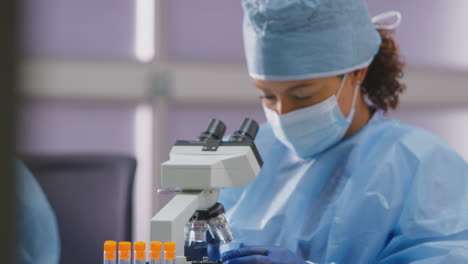 trabajadora de laboratorio que lleva un ppe analizando una diapositiva bajo el microscopio