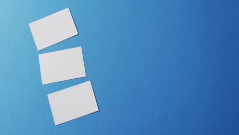 overhead view of three white business cards arranged on blue background, copy space, slow motion