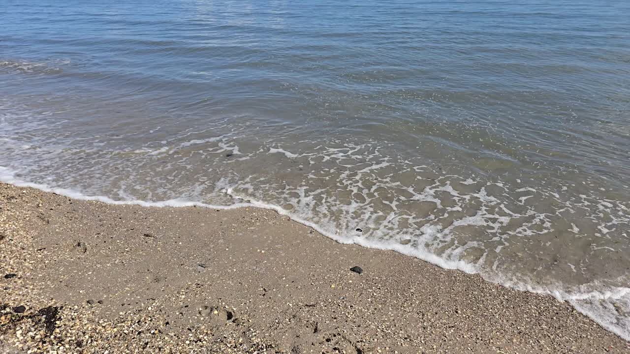 Primer plano de pequeñas olas marinas rompiendo en una playa de arena a cámara lenta