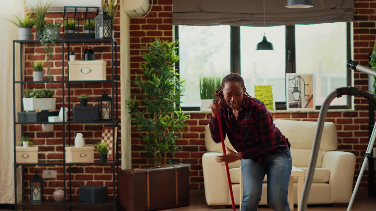 African american housewife listening to music and mopping apartment floors