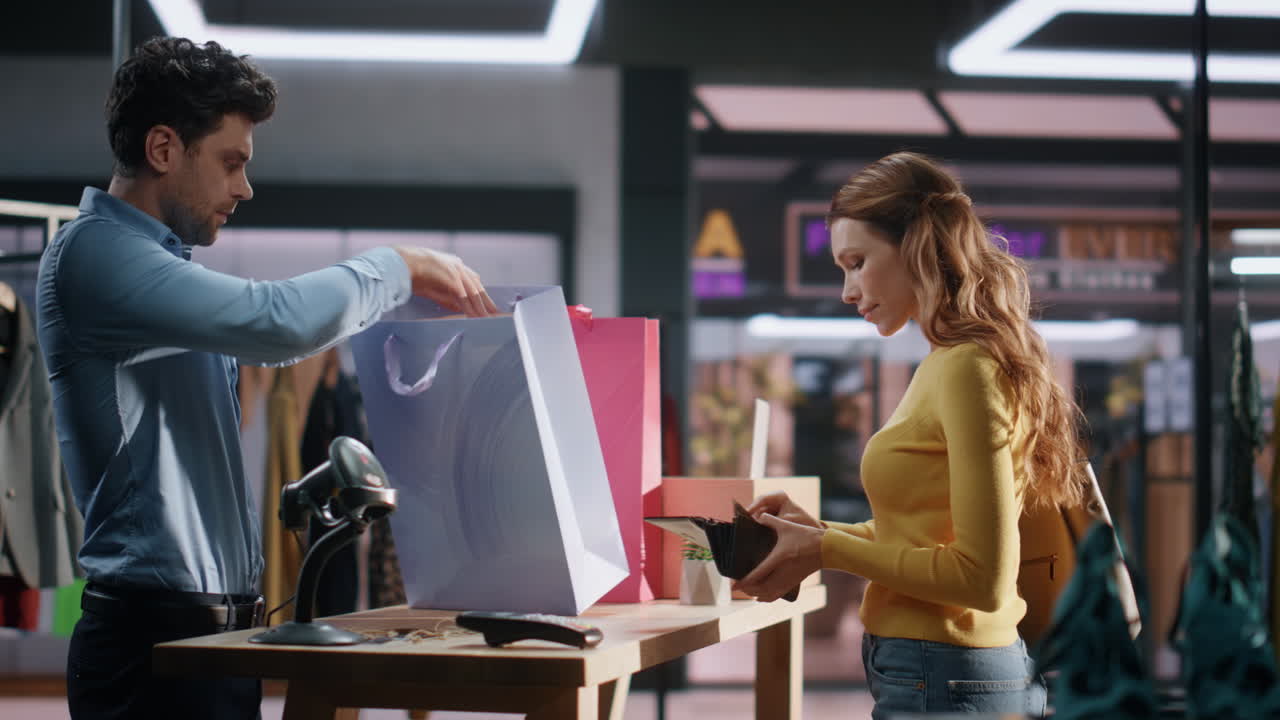 옷 가게에 구매 가방을 넣는 판매자. 즐거운 여자가 물건을 구입합니다.