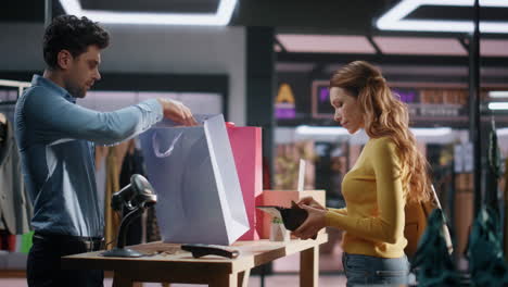 el vendedor pone la bolsa de compras en la tienda de ropa. la mujer alegre compra artículos.