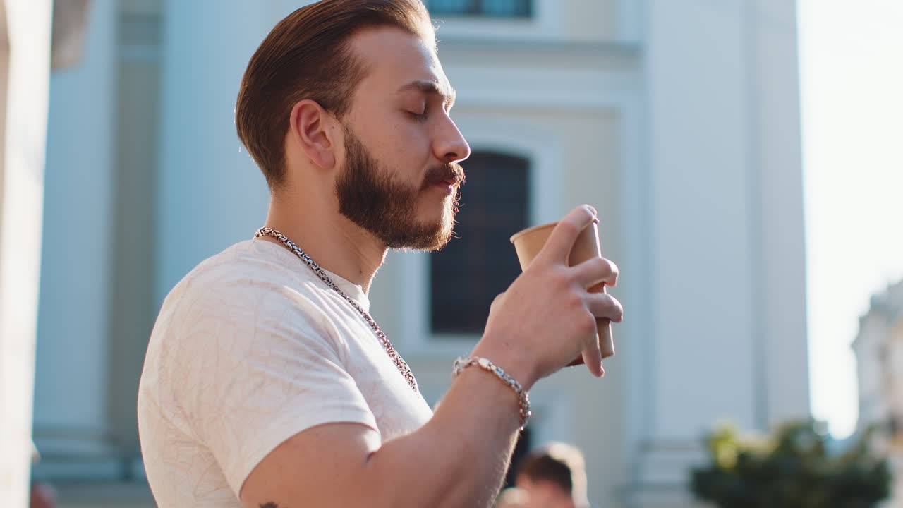 Young man guy enjoying drinking morning coffee hot drink relaxing taking a break in city street