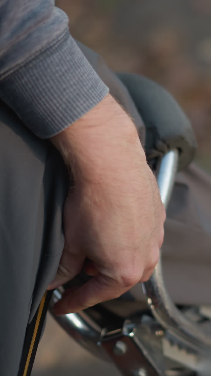 primer plano de una persona con ropa gris ajustando la correa negra y naranja en el zócalo, manos trabajando con enfoque y precisión, fondo al aire libre borroso, enfatizando la acción de asegurar y fijar el equipo