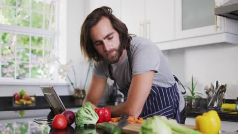 hombre caucásico que usa un delantal usando una tableta digital en la cocina en casa