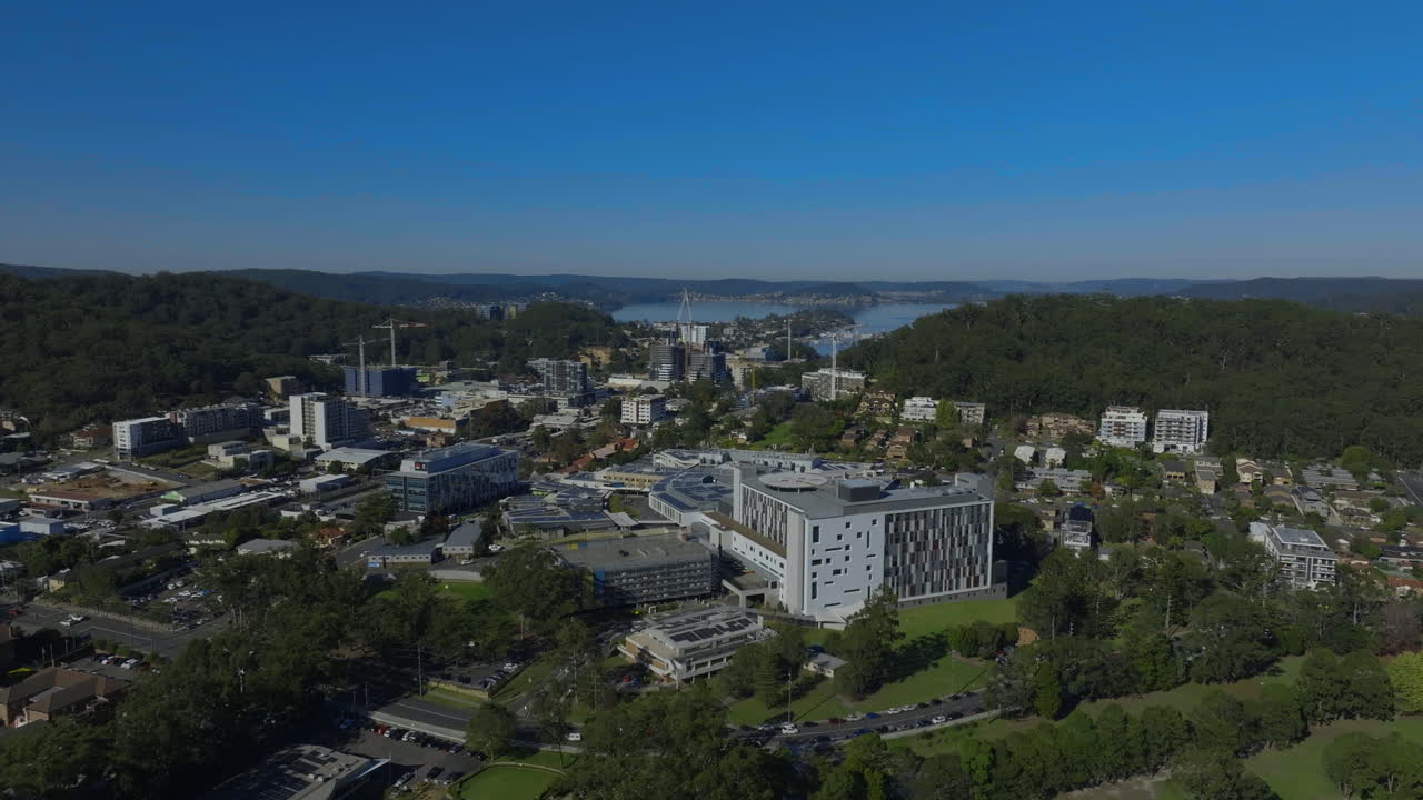 impresionantes imágenes aéreas del hospital de gosford en un soleado día de otoño, mostrando el cbd de gosford y las aguas de brisbane en el fondo, capturando la belleza de la costa central de nsw con un dron.