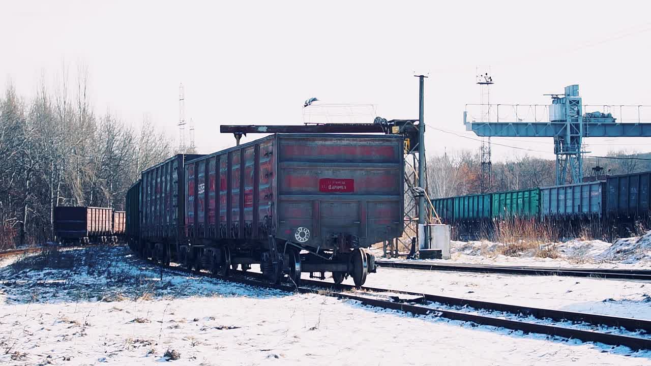 Un antiguo tren de carga con mercancías avanza sobre raíles en un día despejado de nieve
