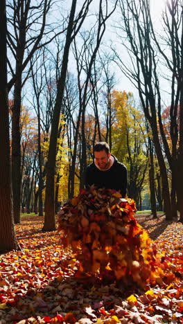 man playing in autumn leaves in a sunny park