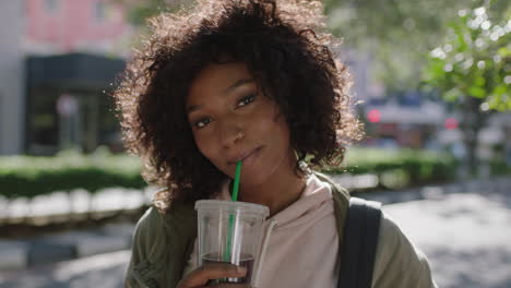 retrato de una joven atractiva mujer afroamericana afro peinado relajado disfrutando de una bebida calle soleada de la ciudad