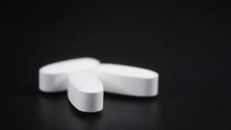 close-up of a single white oval pill on a black background