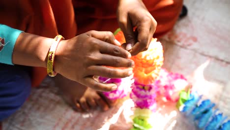 Hands-of-woman-making-traditional-Indian-necklace-with-fabric-flowers-in-Noondpura-village,-Rajasthan