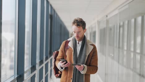 stylish adult man walking down the hall makes a purchase online on a smartphone with a credit card