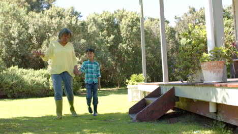 Feliz-Abuela-Birracial-Y-Nieto-Caminando-En-Un-Jardín-Soleado,-Cámara-Lenta,-Espacio-De-Copia