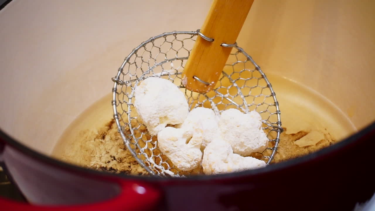 스파이더 스키머로 빵가루를 입힌 콜리플라워를 튀김 기름으로 낮추고 슬로우 모션