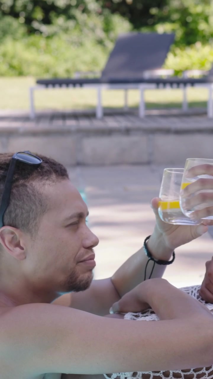Video verticale: Uomo che riceve e prende un bicchiere, donna in crochet bianco che offre limone a bordo piscina, con spazio per il testo.