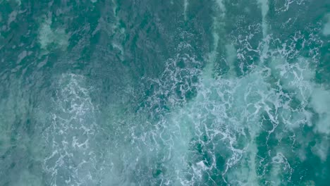 Top-Down-Slow-Motion-Drone-View-of-crystal-clear-water-over-shallow-coral-reef-in-Uluwatu-Bali-Indonesia