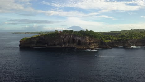 aerial: tourist boat motors out of bay along base of tall sea cliff