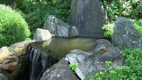 Water-spills-over-the-edge-of-an-ornamental-waterfall-in-a-Japanese-garden