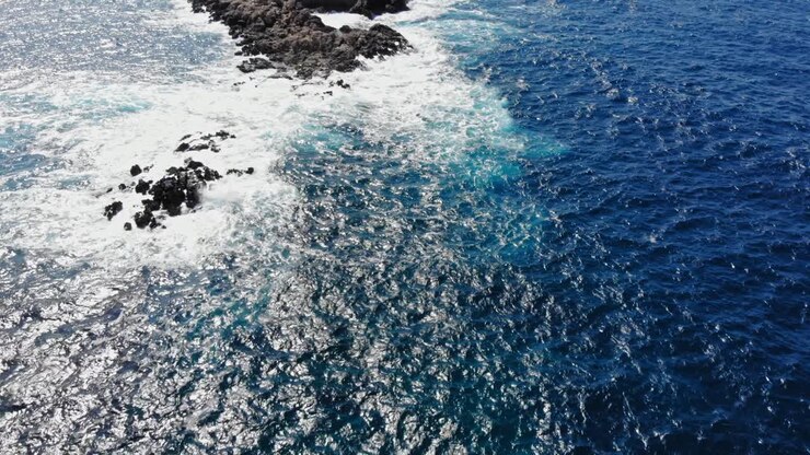 Vista dall'alto di onde marine spumeggianti che si infrangono sulle rocce nel mezzo dell'oceano - ripresa aerea con drone