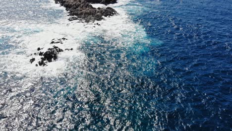 top down view of foamy sea waves splashing on rocks in the middle of the ocean - aerial drone shot