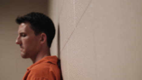 a sad, unhappy, angry prison inmate in orange uniform sitting in cell