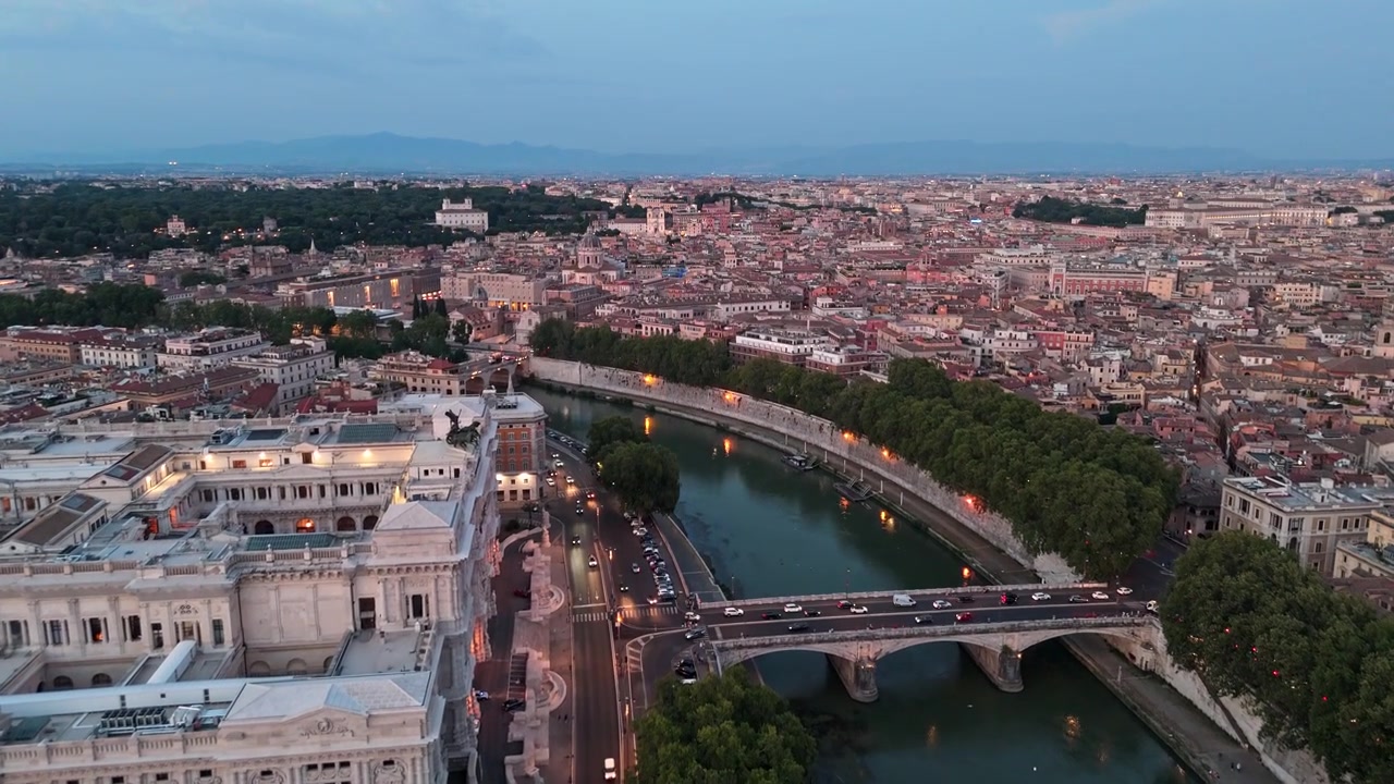 Il Palazzo di Giustizia si affaccia su Ponte Umberto I mentre una ripresa aerea al tramonto sorvola il Tevere e i fitti tetti storici con traffico in movimento