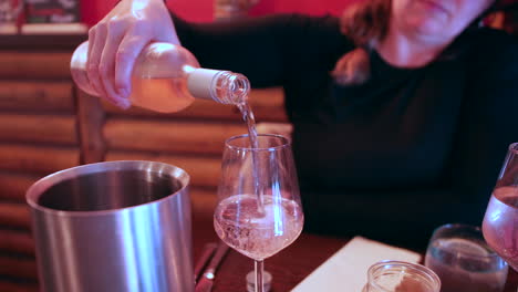 a woman is pouring a bottle of white wine into a wine glass at a dining table