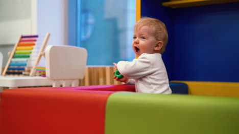 happy little boy child leans on soft edge of playpen in room