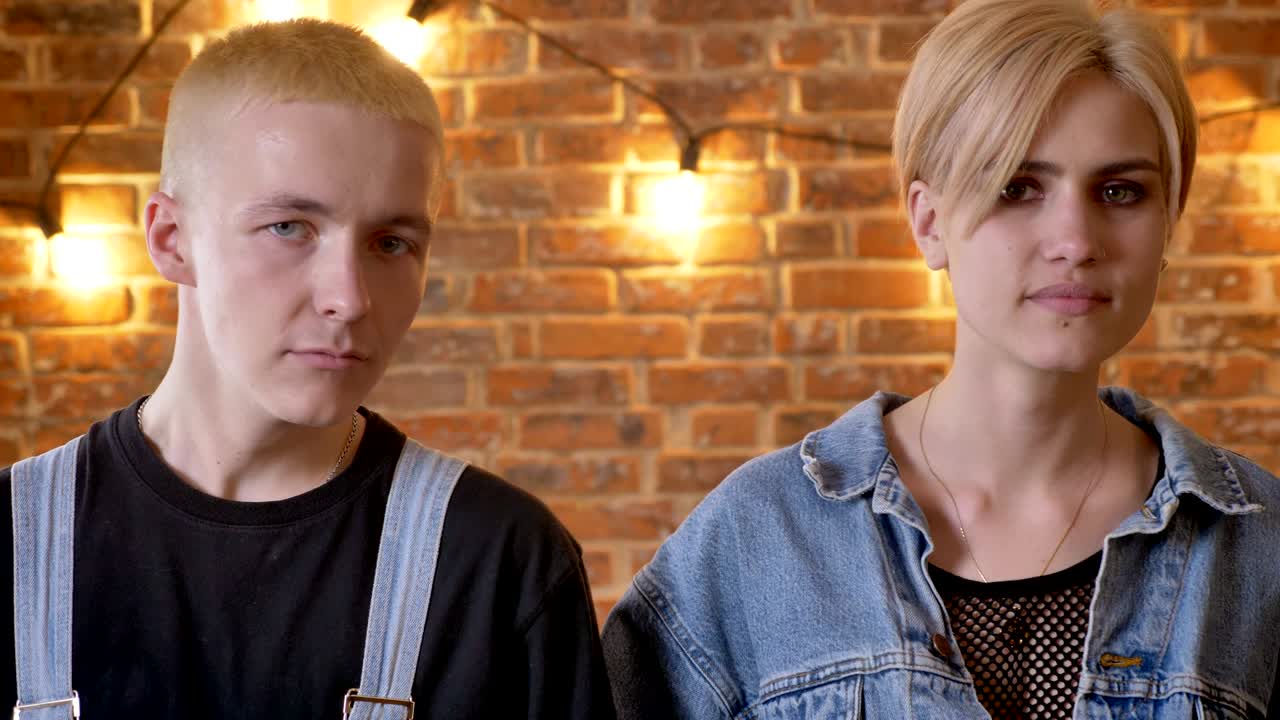 Young cute couple of hipsters is dancing, moving necks, move conception, brick background, close-up