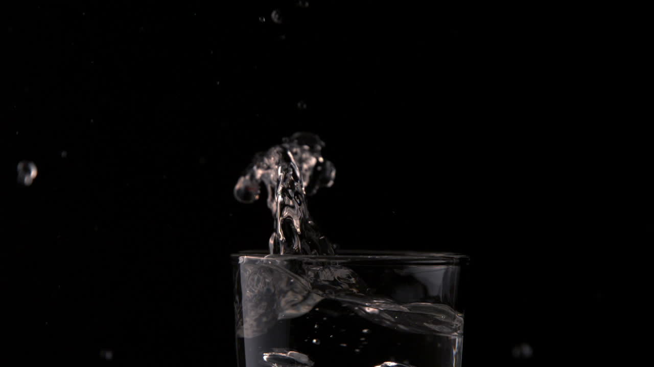 Cubetto di ghiaccio che cade in un bicchiere d'acqua su sfondo nero