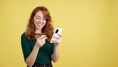 a smiling redheaded woman shopping online with a credit card and smartphone
