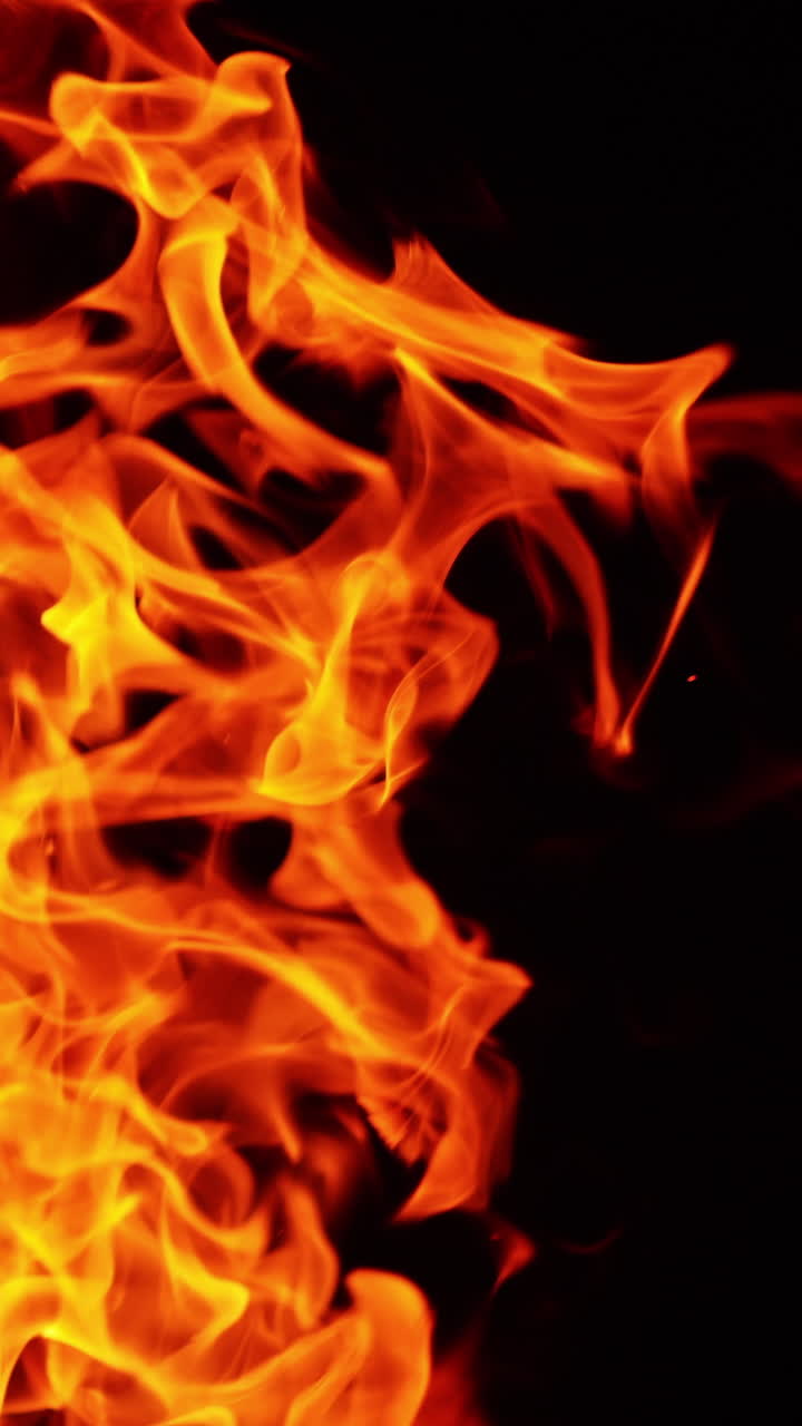 Fiamme e scintille che si protendono verso l'alto. Falò ardente isolato sullo sfondo nero. Video verticale