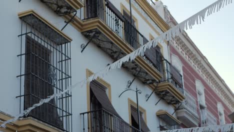 Fachada-De-Edificio-Andaluz-De-ángulo-Bajo,-Banderas-De-Fiesta-Balanceándose-En-La-Brisa