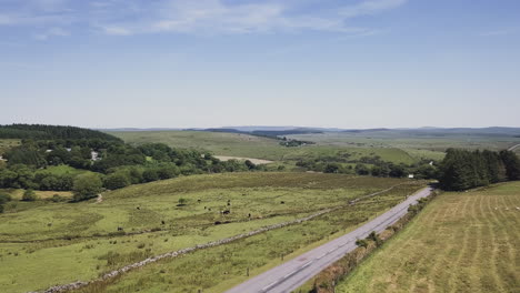 aerial zoom of a paved road through a rural landscape with rolling hills in dartmoor, england