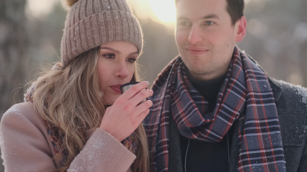 hermosa y elegante pareja de hombre y mujer hipsters con abrigo y bufanda beben té de un termo en el bosque de invierno después de un paseo. historia de amor