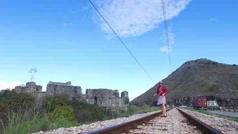 mujer caminando por las vías del tren cerca de antiguas ruinas