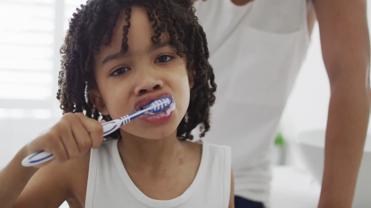 Uomo birazziale felice e suo figlio che si lavano i denti in bagno