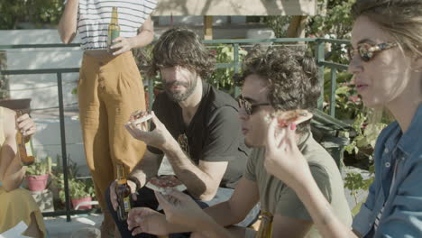 carefree friends drinking beer and eating pizza while sitting on rooftop terrace