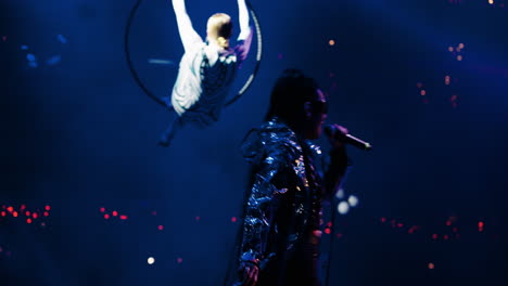 a woman performs aerial silks on stage in front of a cheering crowd