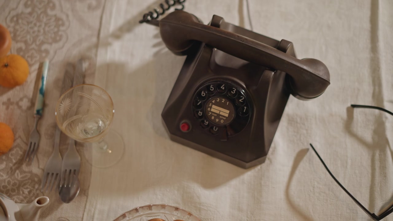 Telefono a disco dall'alto su biancheria con ciotola di pretzel e occhiali, utensili sparsi e penna, atmosfera di studio mattutina, intimo disordine sul tavolo che suggerisce uno scrittore al lavoro e una lenta pausa analogica.