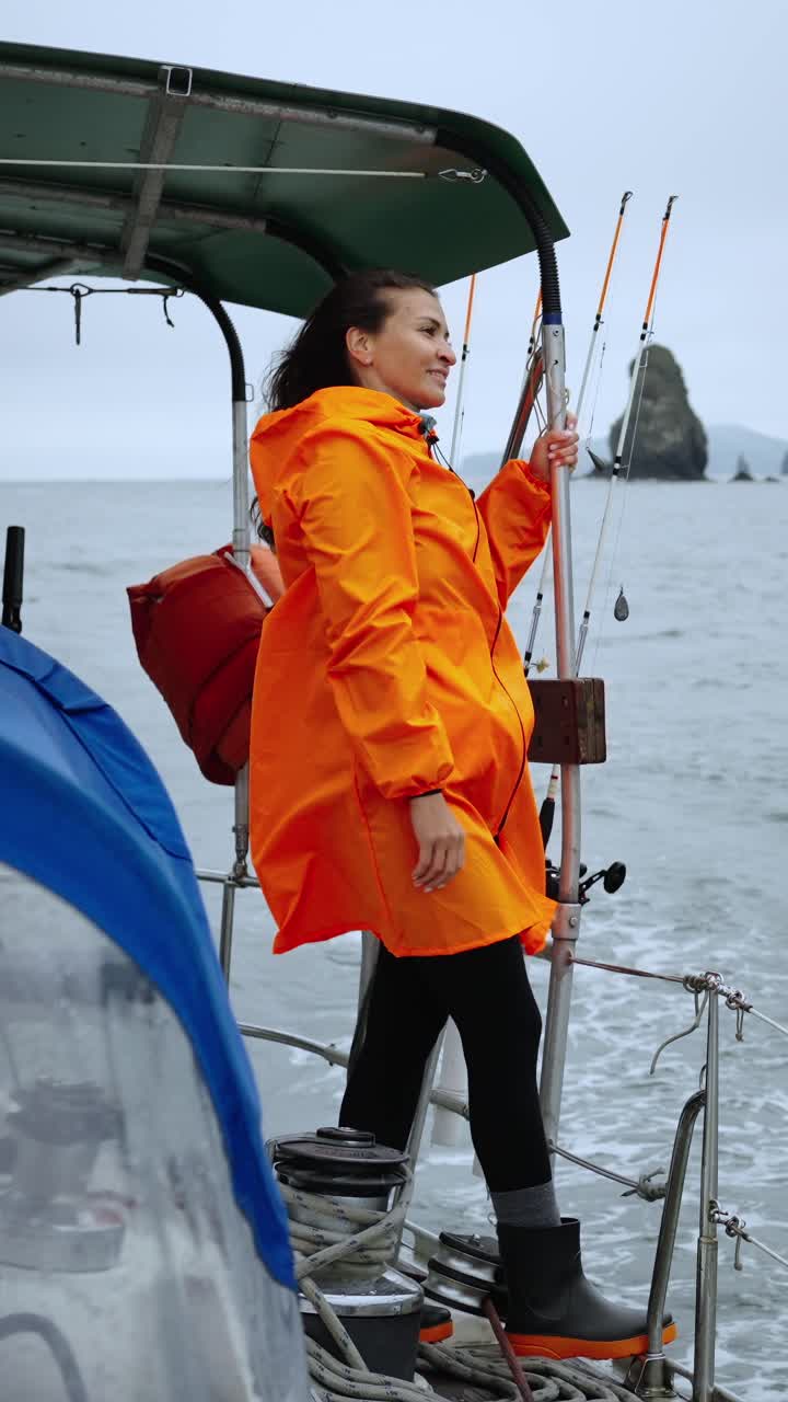 Frau im orangefarbenen Regenmantel steht auf einem Boot auf See