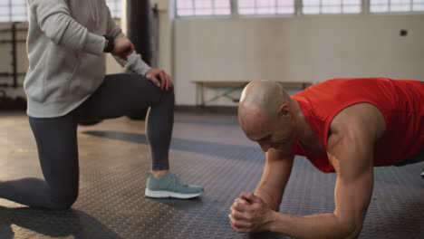 Caucasian-muscular-man-exercising,-doing-plank-with-female-coach