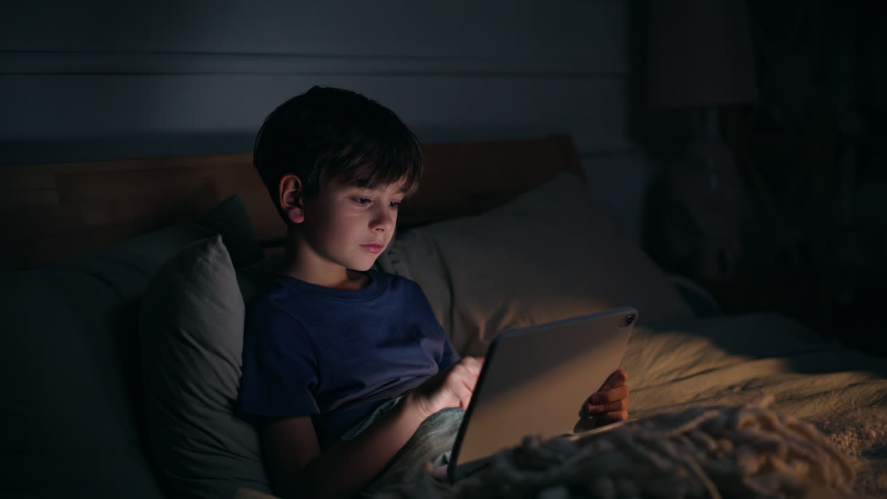 Night boy scrolling tablet lying cozy bedroom closeup. Addicted child touching