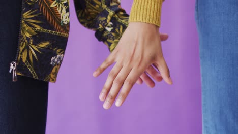 close up of diverse couple holding hands on purple background