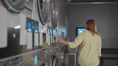 back view employer smiling, sliding hand across industrial washers, tapping controls in modern laundromat, clothes spinning inside, basket on shelf, payment terminal glowing by corner