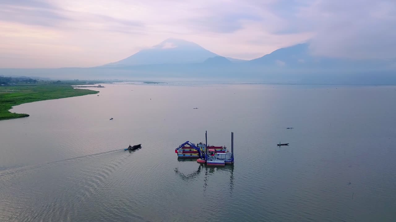 barco de dragado industrial con pluma de grúa en el lago durante el amanecer místico con nubes en asia