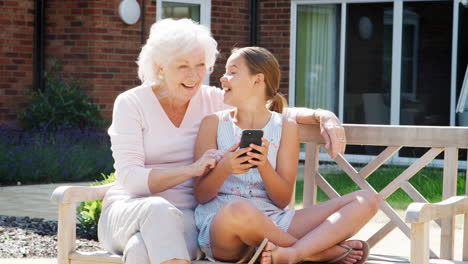 granddaughter showing grandmother mobile phone on visit to retirement home