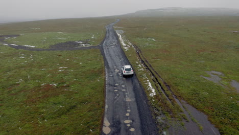 aerial: following a white car on muddy dirt road while snowing