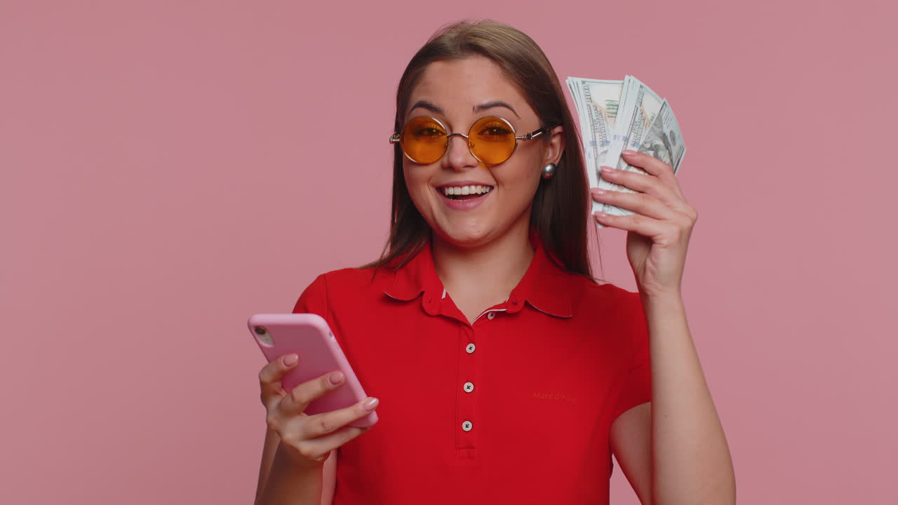 Donna turista felice usa lo smartphone esultando per la vincita, riceve denaro contante in dollari, successo e fortuna alla lotteria.