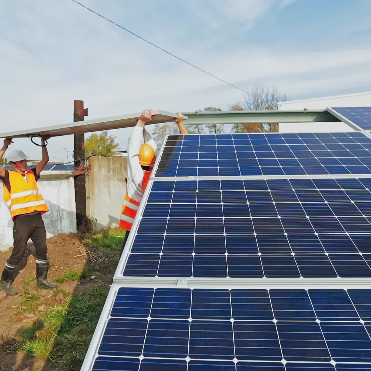 Workers install blue solar panel on the metal basis. Technicians in protective uniform and helmet attach sunny battery. Alternative source of energy.